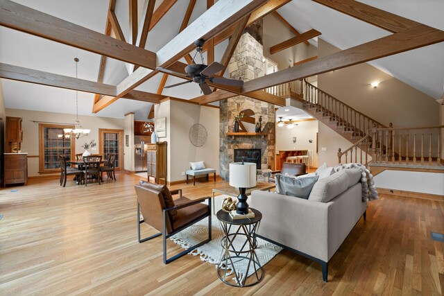 living room with beam ceiling, a stone fireplace, high vaulted ceiling, ceiling fan with notable chandelier, and light hardwood / wood-style floors