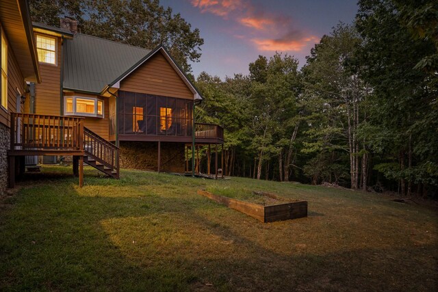 yard at dusk featuring a sunroom and a deck