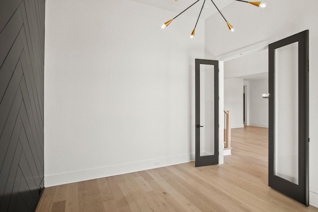 empty room featuring light wood-style floors, baseboards, a chandelier, and french doors