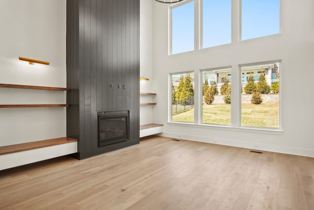 unfurnished living room with a towering ceiling, a large fireplace, baseboards, and wood finished floors