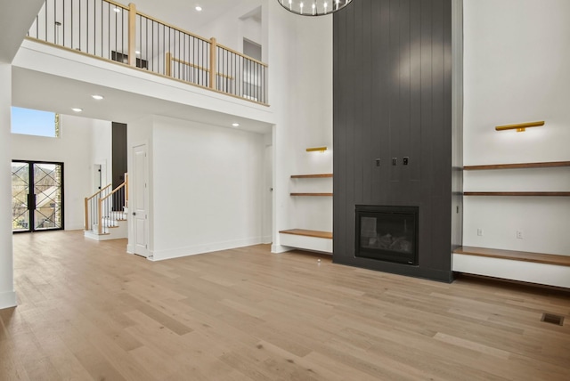 unfurnished living room featuring a large fireplace, visible vents, wood finished floors, a high ceiling, and stairs