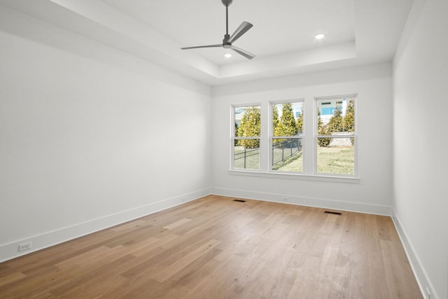 spare room with baseboards, a ceiling fan, a tray ceiling, light wood-type flooring, and recessed lighting