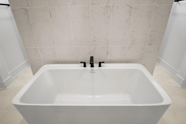 bathroom with marble finish floor, a bathing tub, baseboards, and tile walls