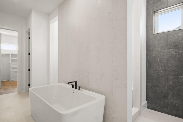 full bathroom with tile walls, a spacious closet, tiled shower, a soaking tub, and tile patterned floors