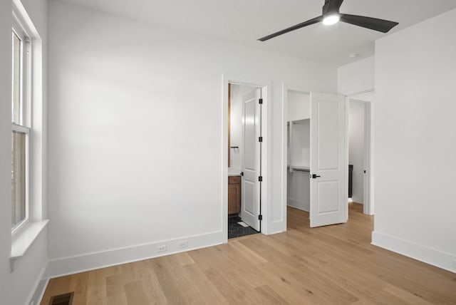 unfurnished bedroom with visible vents, baseboards, ensuite bath, a spacious closet, and light wood-style floors