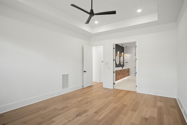 unfurnished room with a tray ceiling, recessed lighting, visible vents, light wood-style floors, and baseboards