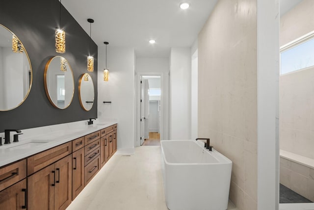 full bath featuring double vanity, a freestanding tub, a sink, and recessed lighting