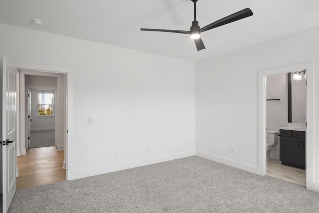 unfurnished bedroom with light colored carpet, connected bathroom, baseboards, and ceiling fan