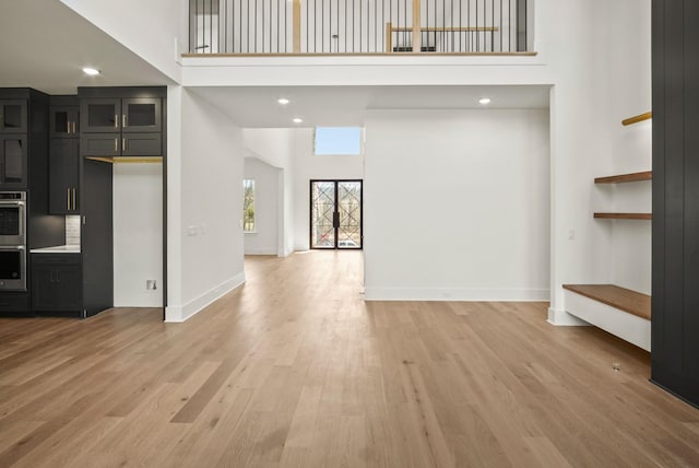 unfurnished living room with light wood-style flooring, recessed lighting, a towering ceiling, and baseboards