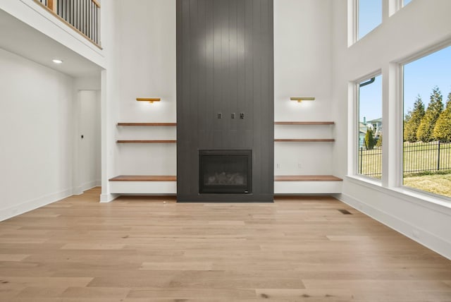 unfurnished living room featuring baseboards, a fireplace, a high ceiling, and wood finished floors