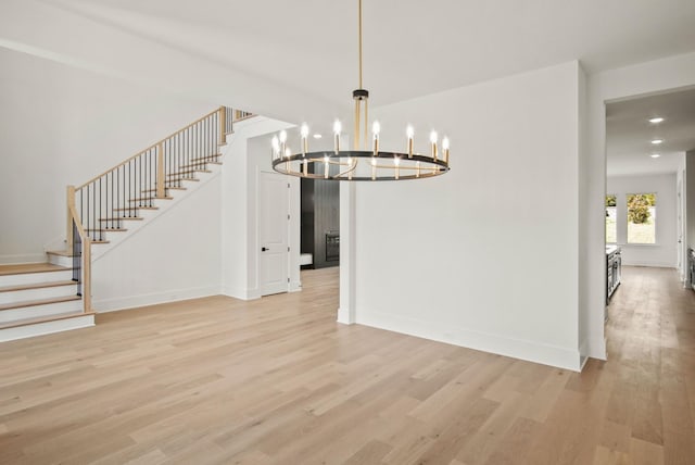 unfurnished dining area with light wood-style floors, an inviting chandelier, baseboards, and stairs