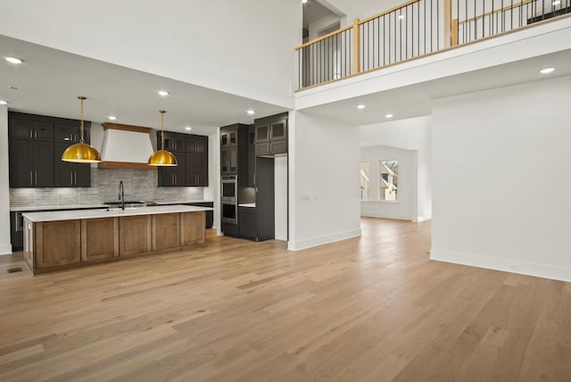 kitchen with light wood-style flooring, a sink, open floor plan, light countertops, and custom exhaust hood