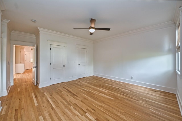 unfurnished bedroom featuring crown molding, baseboards, light wood-type flooring, and two closets