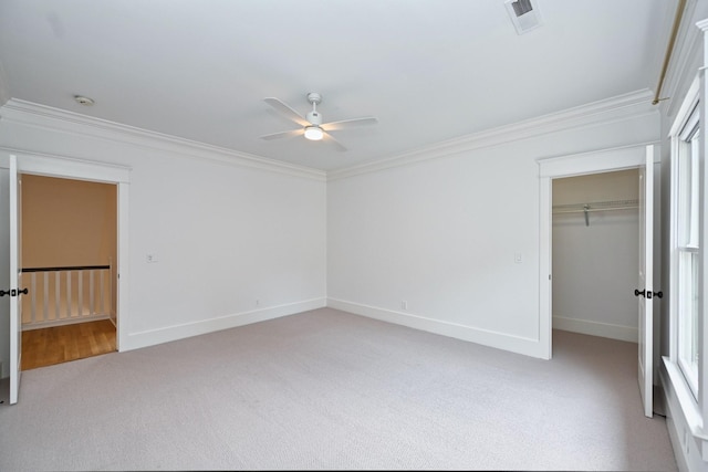 unfurnished bedroom featuring visible vents, light carpet, a closet, crown molding, and a spacious closet