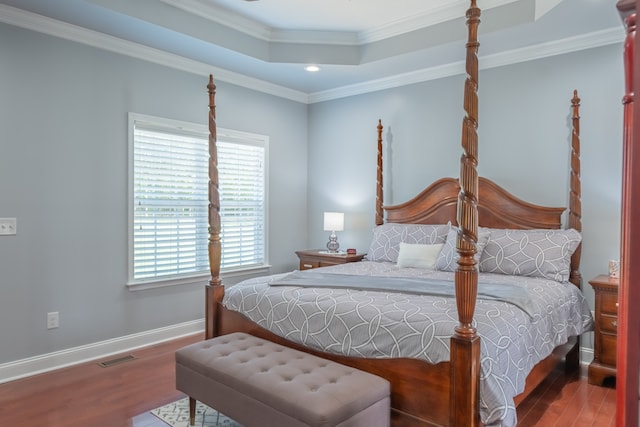 bedroom with hardwood / wood-style flooring, a raised ceiling, and crown molding