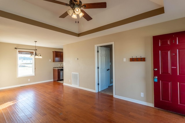 unfurnished living room with a tray ceiling, baseboards, visible vents, and wood finished floors