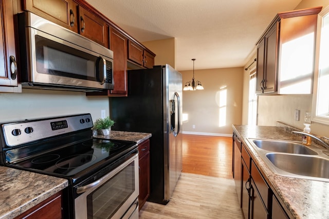 kitchen with decorative light fixtures, light wood finished floors, stainless steel appliances, a sink, and a chandelier