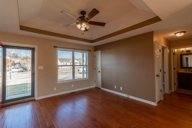 empty room with plenty of natural light, baseboards, a raised ceiling, and wood finished floors