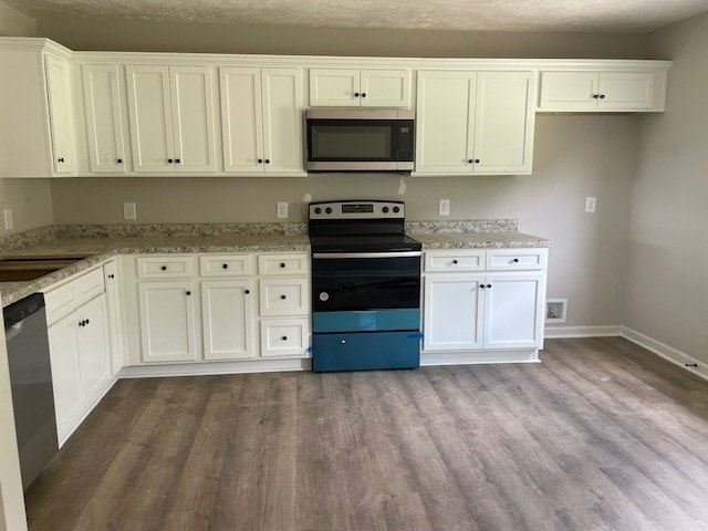 kitchen featuring white cabinets, stainless steel appliances, light stone countertops, and hardwood / wood-style floors