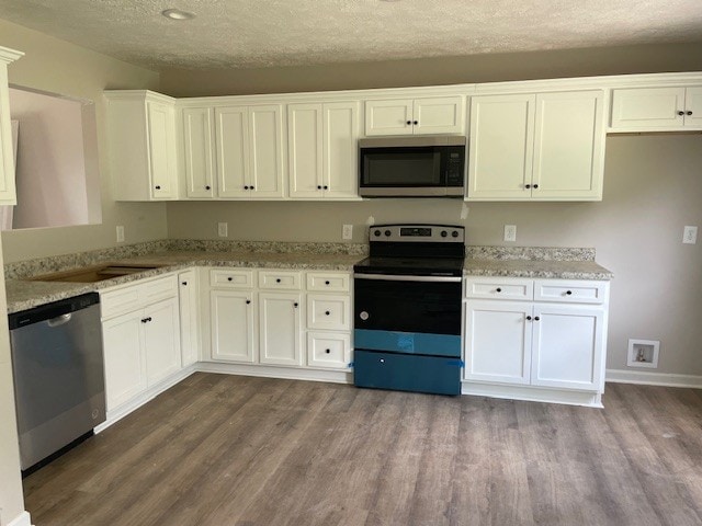 kitchen with white cabinetry, light stone counters, stainless steel appliances, and hardwood / wood-style floors