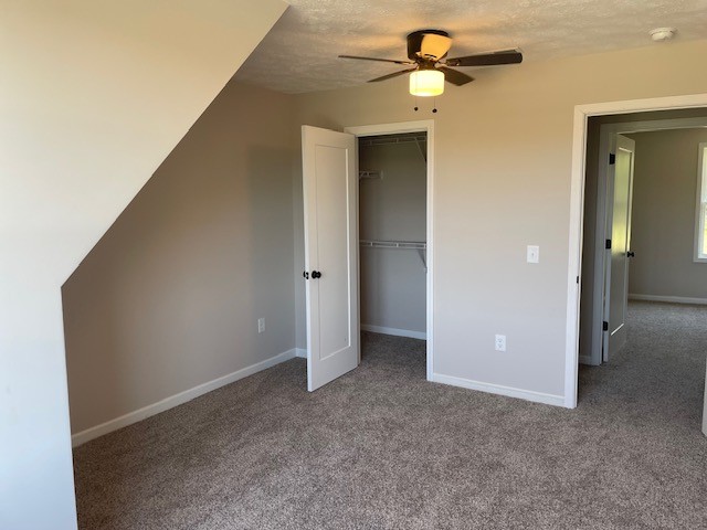 unfurnished bedroom featuring a closet, ceiling fan, a textured ceiling, and carpet floors