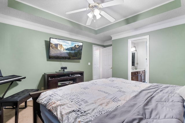 bedroom featuring a ceiling fan, carpet floors, ensuite bath, a tray ceiling, and ornamental molding