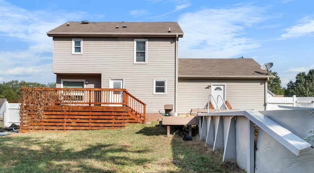 back of property with a shingled roof, a wooden deck, a yard, and fence