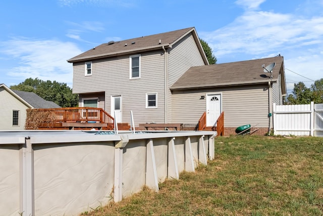 back of property with a deck, fence, a yard, roof with shingles, and an outdoor pool