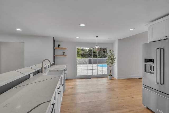 kitchen with light hardwood / wood-style floors, white cabinetry, light stone countertops, high quality fridge, and sink