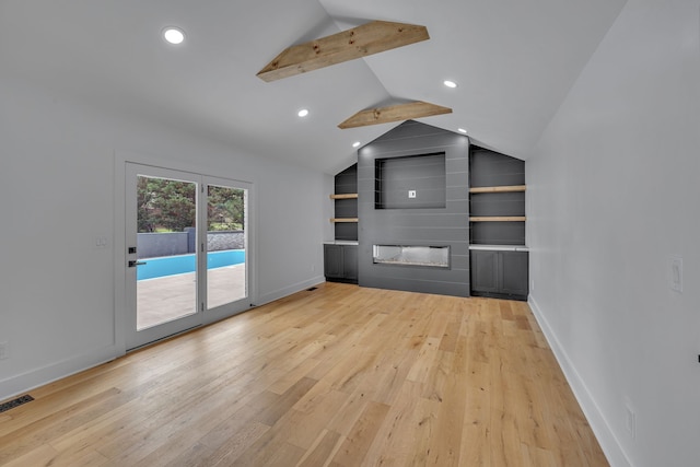 unfurnished living room with lofted ceiling with beams, a large fireplace, built in shelves, and light wood-type flooring