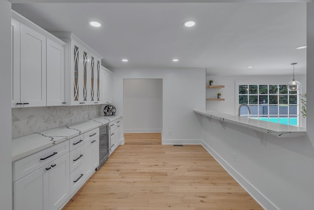 kitchen featuring pendant lighting, white cabinets, light wood-type flooring, and tasteful backsplash