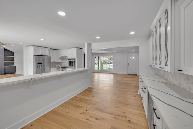 kitchen with appliances with stainless steel finishes, a kitchen bar, light hardwood / wood-style floors, and white cabinets