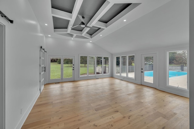 unfurnished living room with light wood-type flooring, beam ceiling, a barn door, and high vaulted ceiling