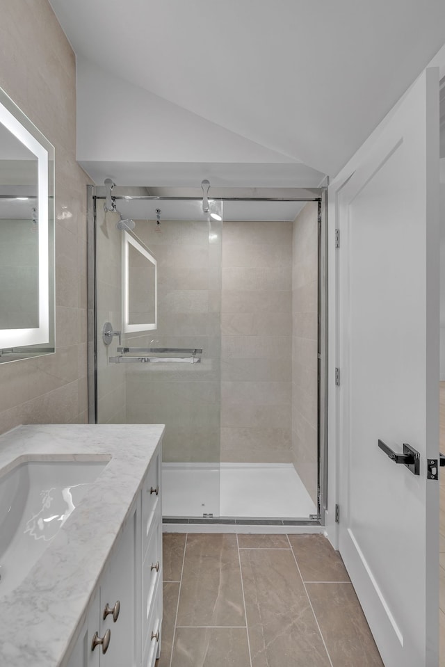 bathroom with walk in shower, lofted ceiling, vanity, and tile patterned flooring