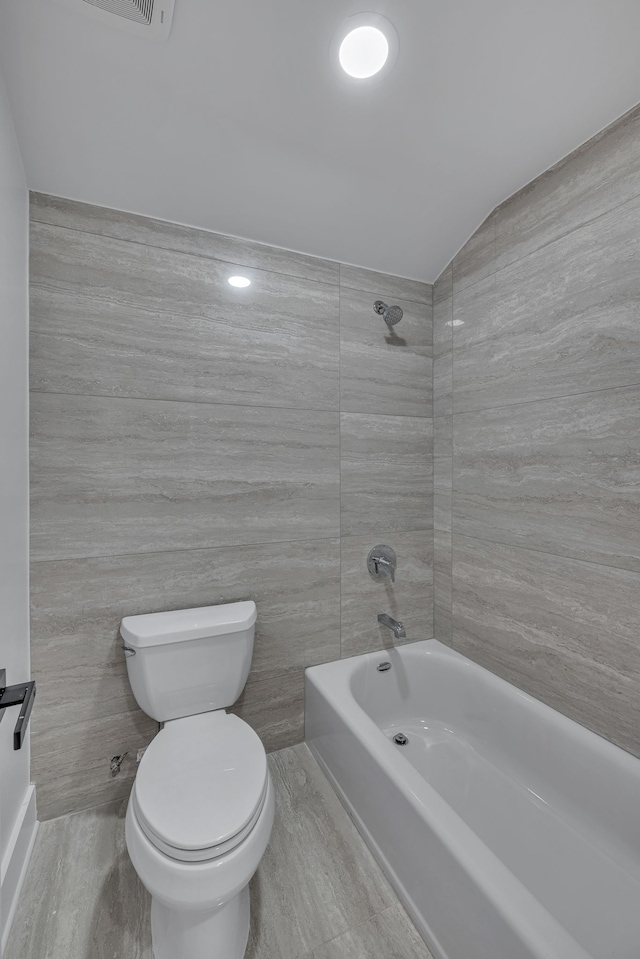 bathroom featuring tile walls, bathing tub / shower combination, and toilet