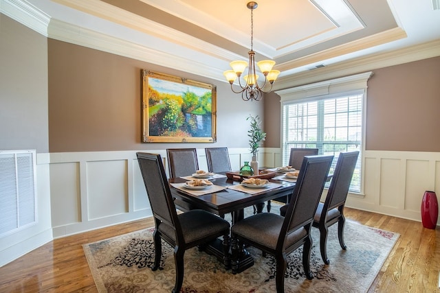 dining area featuring crown molding, a raised ceiling, hardwood / wood-style floors, and an inviting chandelier