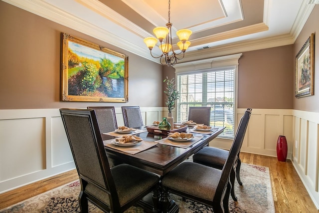 dining area with crown molding, an inviting chandelier, light hardwood / wood-style flooring, and a tray ceiling