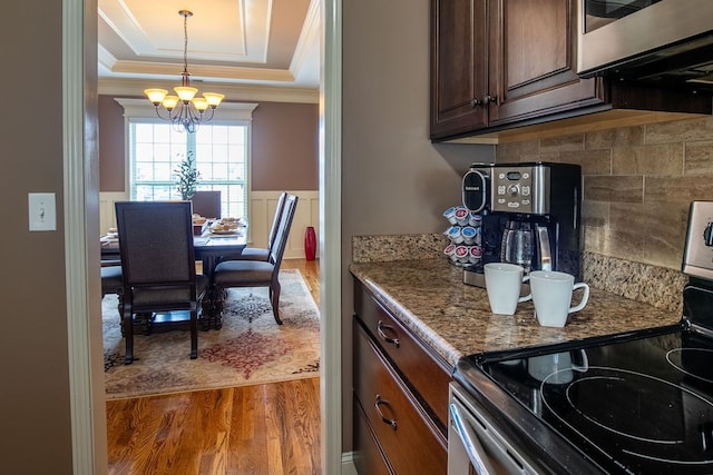 kitchen with hanging light fixtures, appliances with stainless steel finishes, a chandelier, a tray ceiling, and dark wood-type flooring