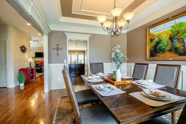 dining space featuring ceiling fan with notable chandelier, a tray ceiling, dark hardwood / wood-style flooring, and ornamental molding