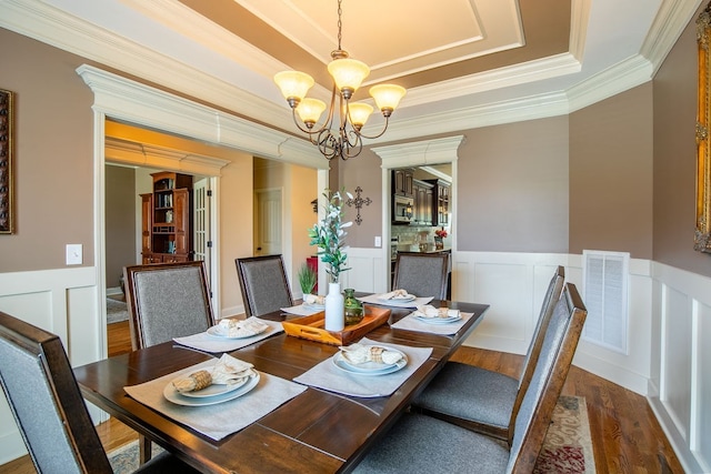 dining room featuring a tray ceiling, hardwood / wood-style flooring, crown molding, and a chandelier