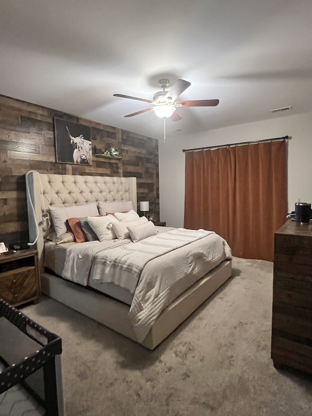 carpeted bedroom featuring wood walls and ceiling fan