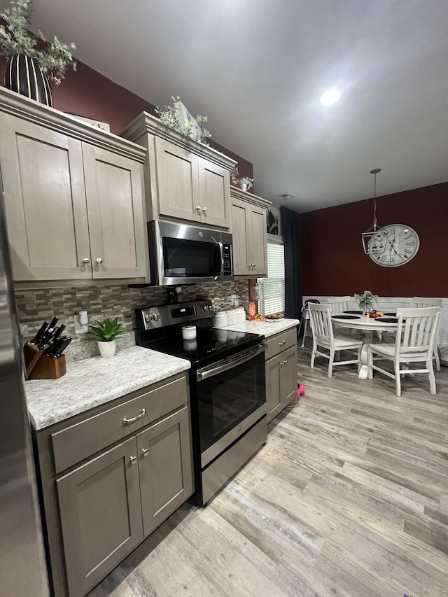 kitchen featuring light hardwood / wood-style flooring, appliances with stainless steel finishes, hanging light fixtures, and tasteful backsplash