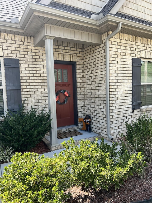 view of exterior entry with roof with shingles