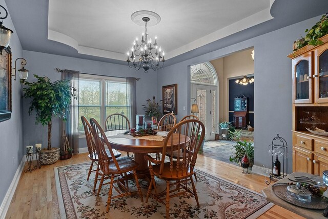 dining space featuring an inviting chandelier, a raised ceiling, and light hardwood / wood-style flooring