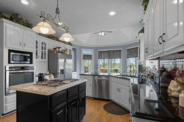 kitchen with a kitchen island, sink, a tray ceiling, appliances with stainless steel finishes, and light hardwood / wood-style floors