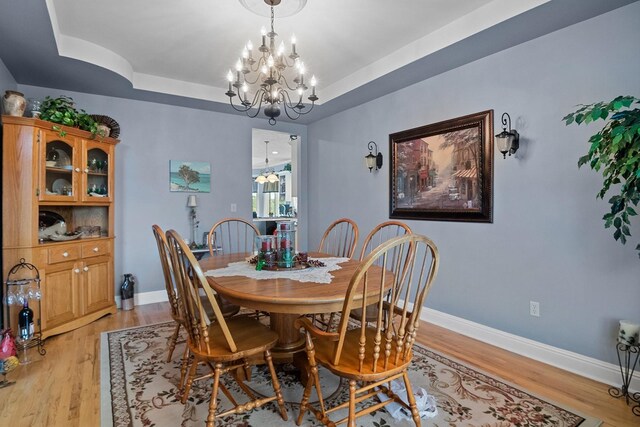 dining room featuring a raised ceiling, a chandelier, and light hardwood / wood-style floors