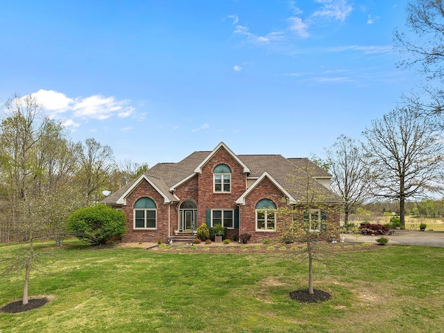 traditional-style home with a shingled roof, a front yard, and brick siding