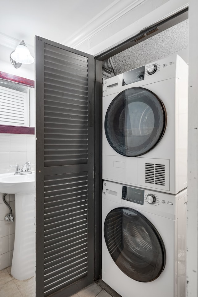 washroom featuring tile walls, light tile patterned floors, and stacked washer / drying machine