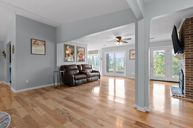 living room with light wood-type flooring, a healthy amount of sunlight, ceiling fan, and a brick fireplace