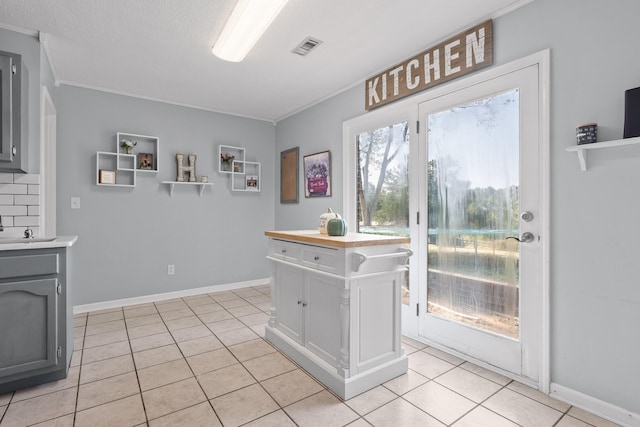 kitchen featuring light tile patterned flooring, ornamental molding, gray cabinets, and tasteful backsplash